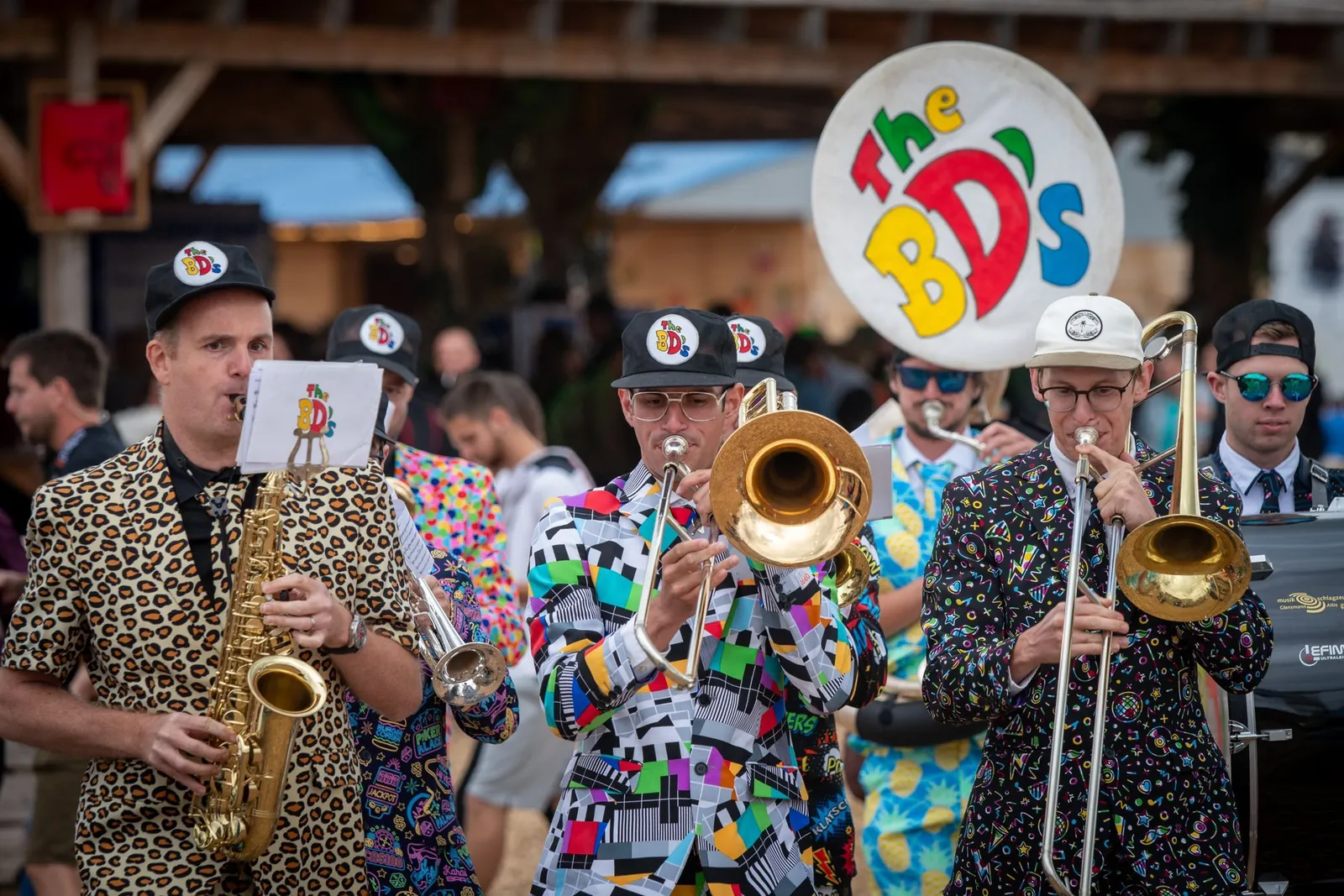 Les BD’s en costumes léopard et bariolés, saxophone et trombones en avant, sous le panneau au logo