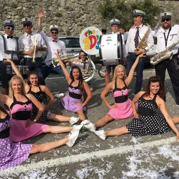 La bande en chemises blanches et casquettes, avec des danseuses en robes roses assises devant elle