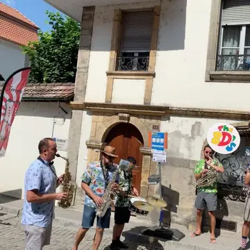 Trois musiciens des BD's jouent devant une maison, à côté du panneau au logo
